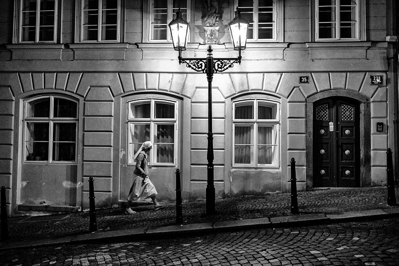 A pedestrian passing a street lamp and an old façade at night